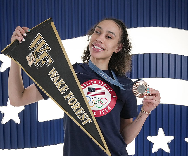 Photo of Dearica Hamby holding Wake Forest pennant and an Olympic Bronze Medal.