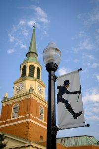 A Demon Deacon banner with a cloth mask hangs on Hearn Plaza in front of Wait Chapel, on the campus of Wake Forest University, Wednesday, May 26, 2021.