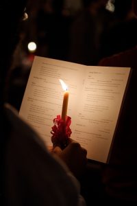 A person reads the Lovefeast program by the light of their Lovefeast candle.