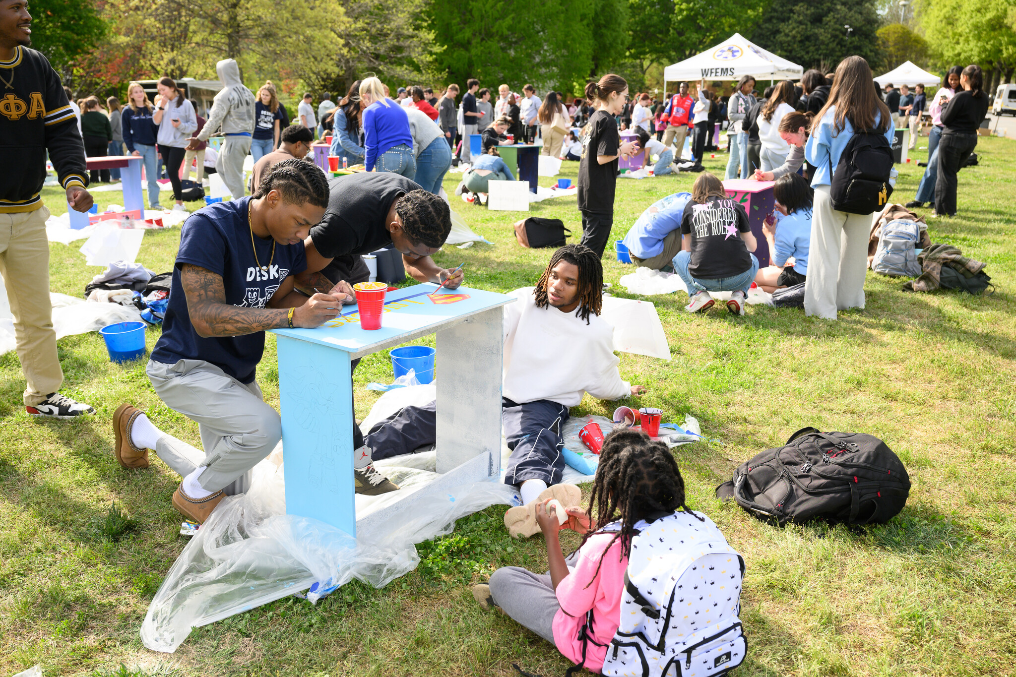 Wake Forest University students paint desks alongside local school children at Davis Field on Wednesday, April 8, 2026 as part of Discovering Education through Student Knowledge (DESK). The event brings local elementary school children to campus each spring to create inspiring, colorful study spaces for students in their homes. A longstanding campus tradition, DESK was started in 2001 in partnership with Old Town Elementary after two WFU students identified a lack of workspace in the homes of the children they were tutoring.