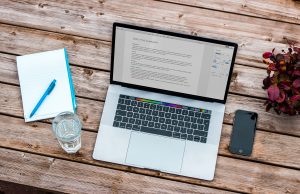 Laptop sitting on a desk with a phone, glass of water, and a calendar planner