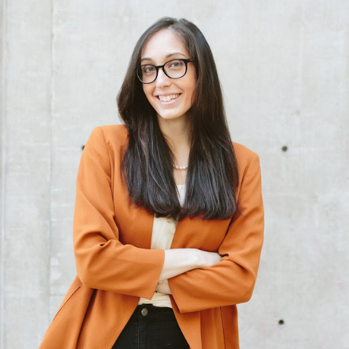 Headshot of Cary Lambert, she is wearing an orange blazer with arms crossed and a big smile