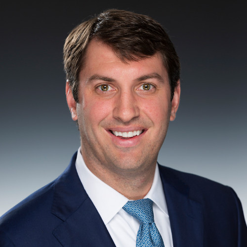 Headshot of James Bailey, he is wearing a suit, blue tie and big smile