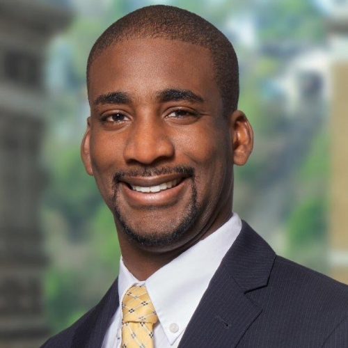 Headshot of Tim Pope, he is wearing a dark suit and golden tie, and a big smile