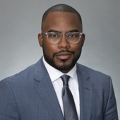 Headshot of Kevin Smith, he is wearing a light blue suit and clear rimmed glasses