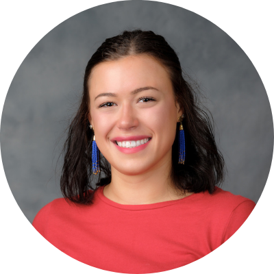 headshot of Natalie Wilson, she has short brown hair and is wearing fun earrings, a bright coral shirt and a big smile