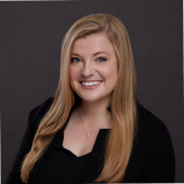 Katie Hooper Headshot, she has long blonde hair and is wearing a black suit