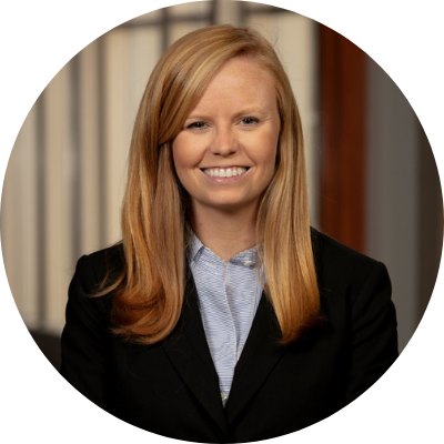 Headshot of Sydney Bailey. She has long, blonde hair and is wearing a black suit jacket, blue shirt, and a big smile.