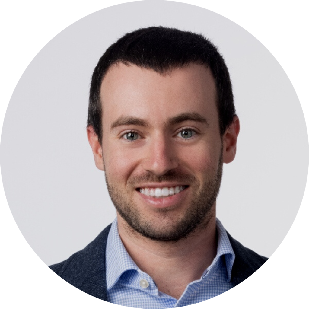 Man with dark hair smiling for a head shot photo wearing a button-up shirt and navy blazer