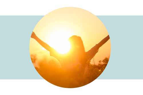 Woman facing the sunshine outside with arms raised in the air