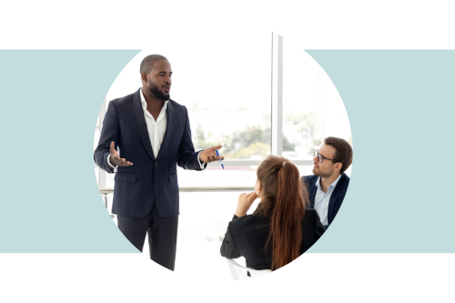 Man in black suit standing up and talking to colleagues in a meeting room