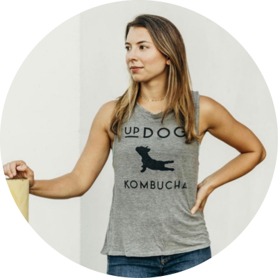 Photo of Olivia Wolff, with brown hair wearing a gray UpDog Kombucha shirt. 