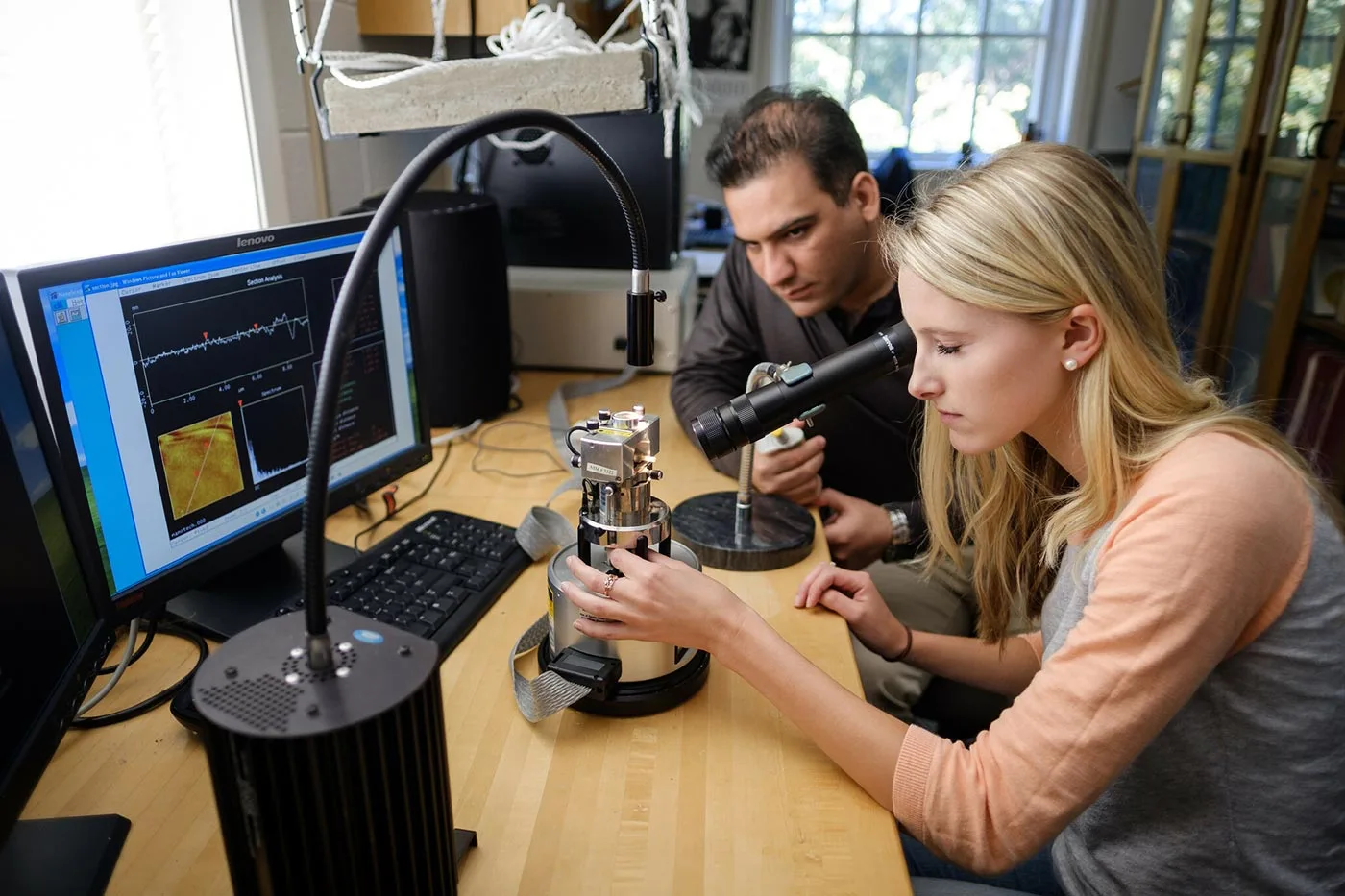 Wake Forest biophysics student works with a graduate student at an atomic force microscope in a physics lab.