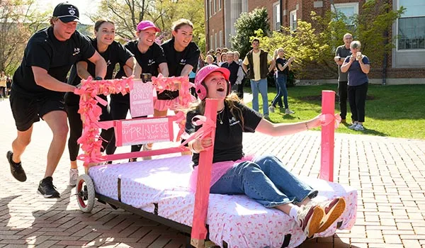 Students participate in a bed race on campus during a student life event.
