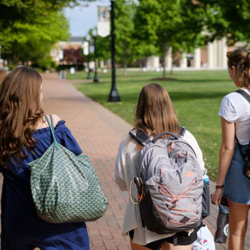 students walk along campus sidewalk with backpacks on