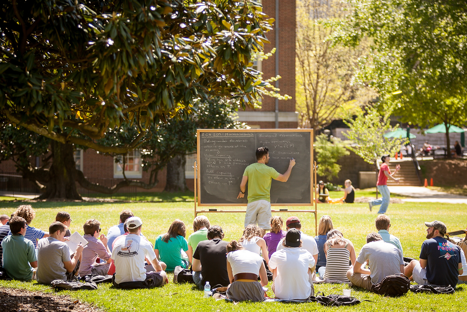 Teacher at blackboard with students in lawn