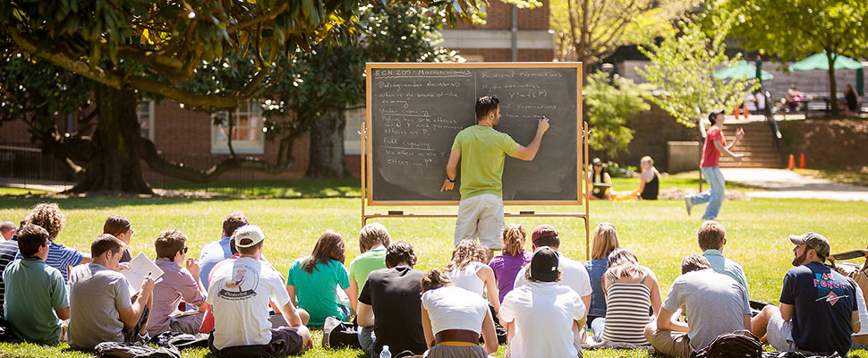 Teacher at blackboard with students in lawn