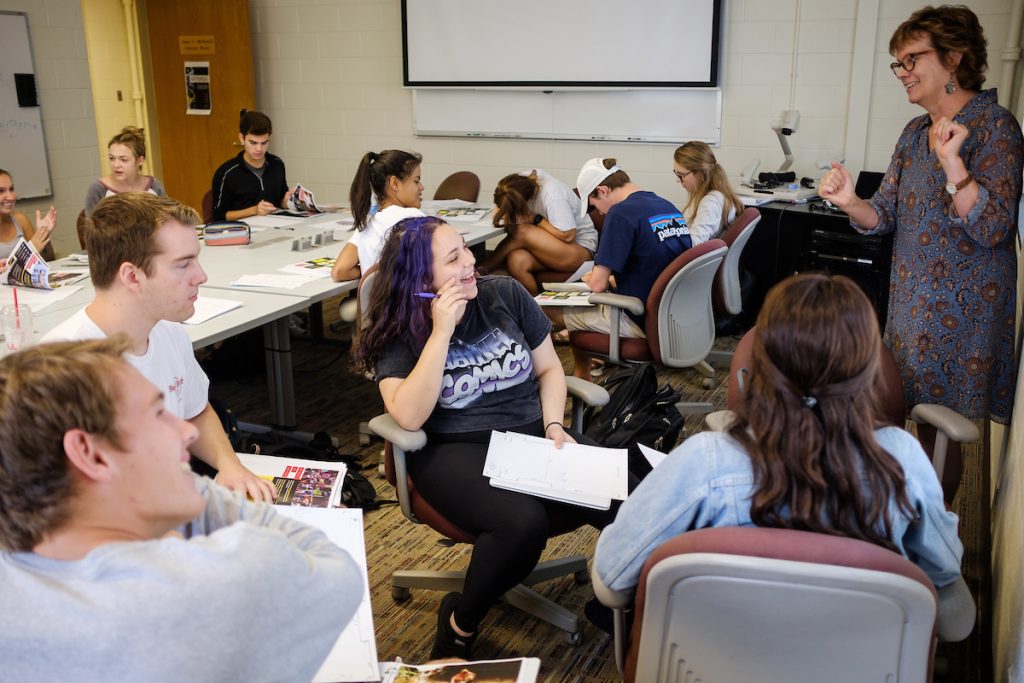 Students sit in desks looking up to Professor Pat Lord who is gesturing.