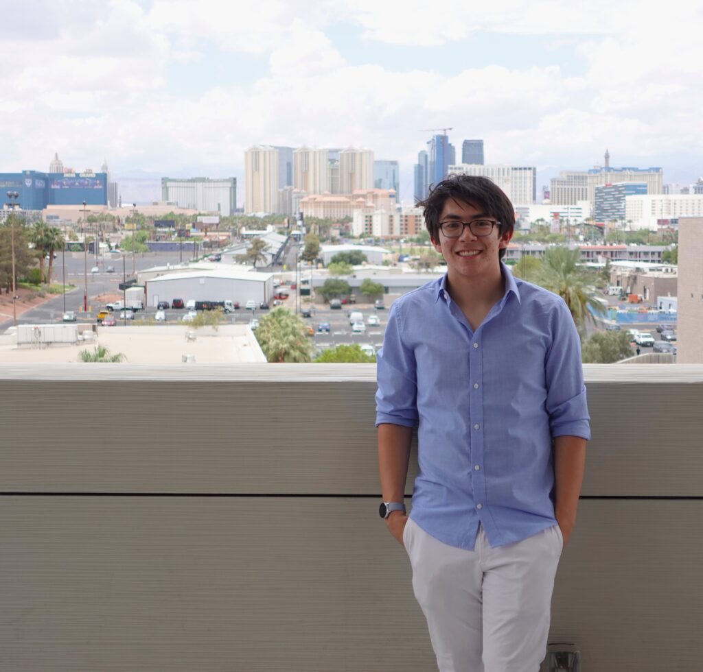 Jae leans against a balcony wearing a blue shirt and white pants.