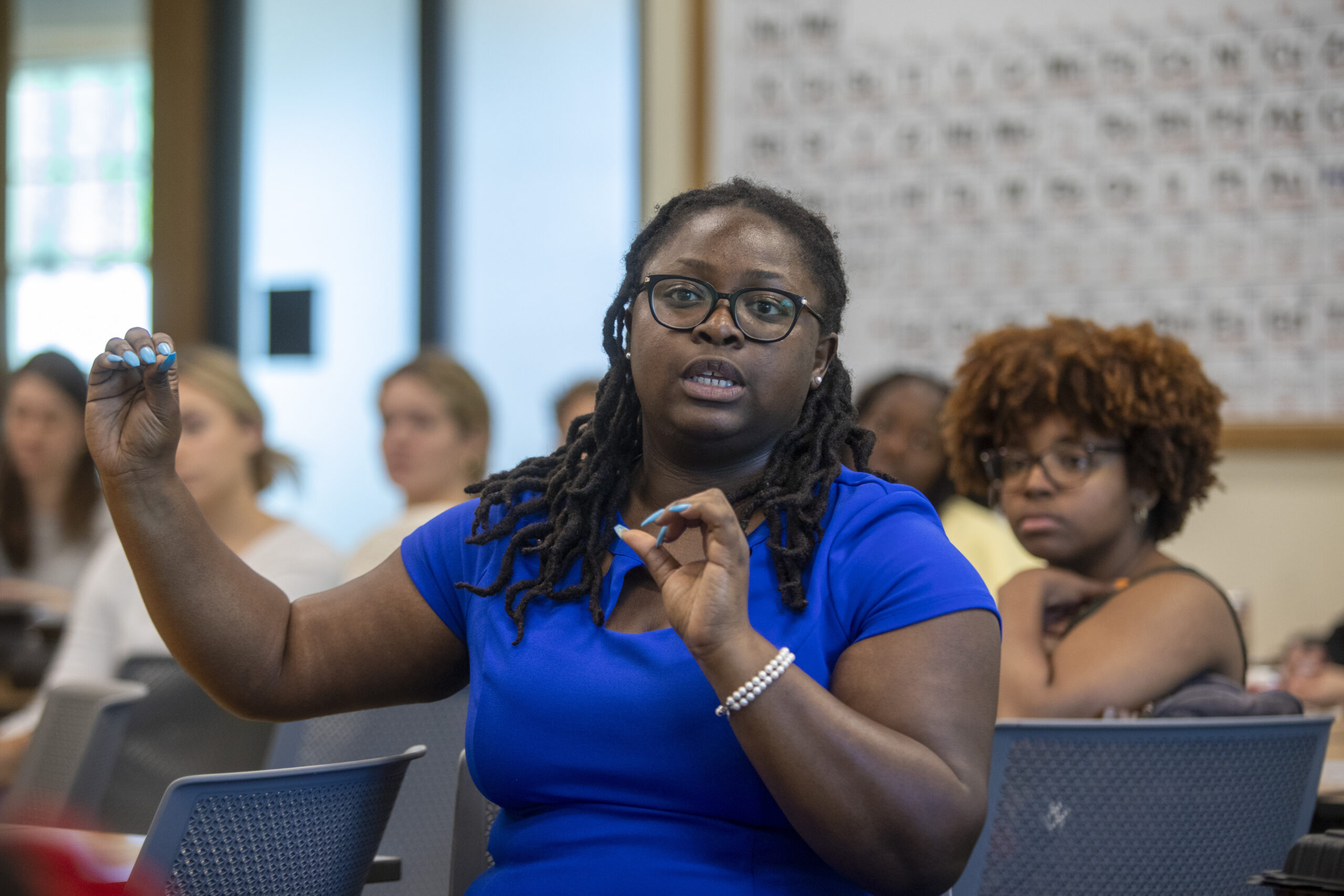 Dr. Ariel Smith, wearing a bright blue shirt, sits in the classroom addressing her students in her Black Entrepreneurship course.