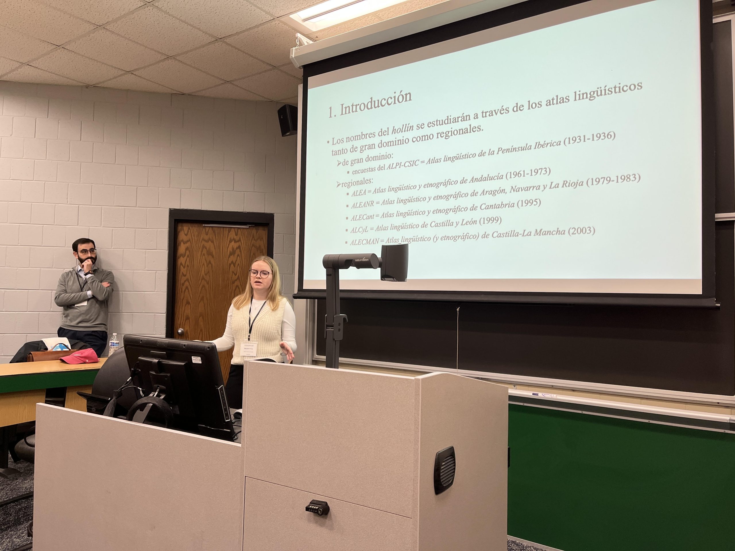 Meredith Prince stands at the front of the classroom with her presentation on a white screen behind her.