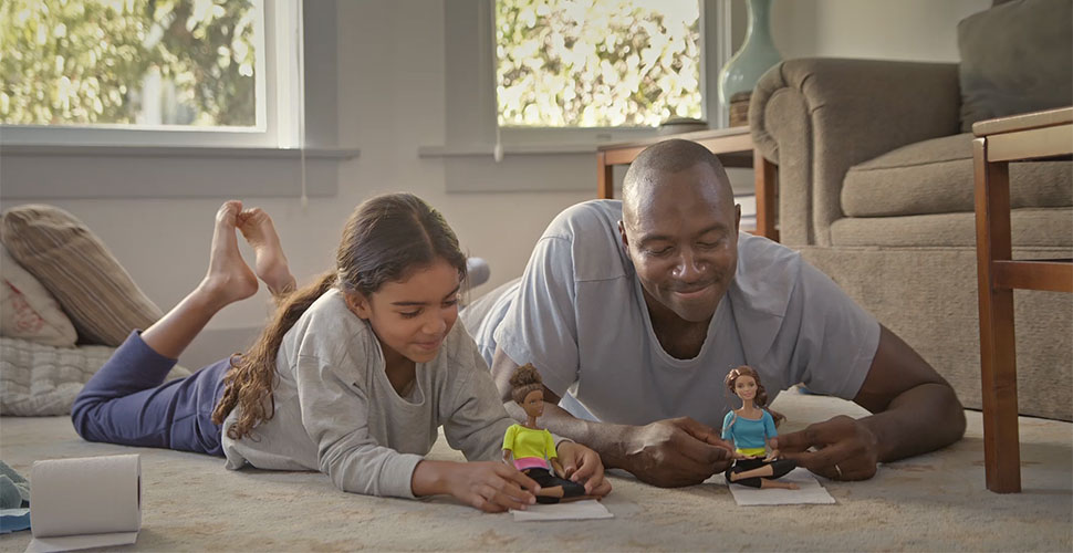 An image of a father and daughter playing with Barbies in a Barbie commercial.