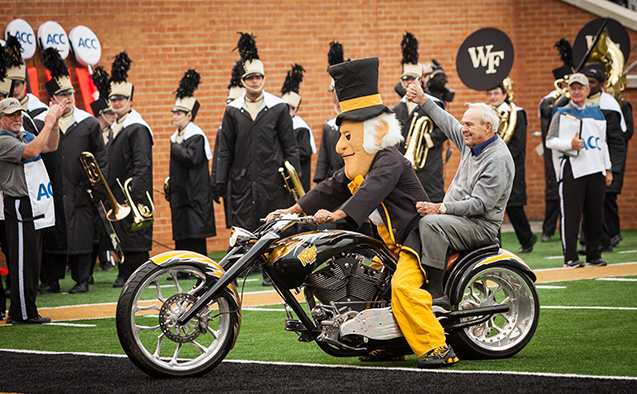 Arnold Palmer riding the motorcycle with the Demon Deacon