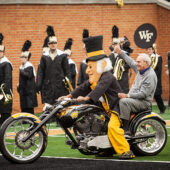 Arnold Palmer riding the motorcycle with the Demon Deacon