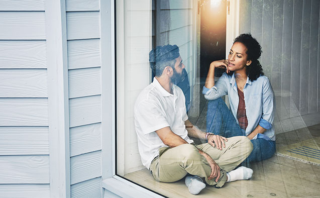 A couple talks in a hallway near a window.