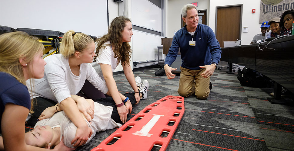 Wake Forest engineering students learn how to use a backboard for spinal injuries, one of several topics they will study this semester in hopes of improving care and outcomes, at Wake Downtown.