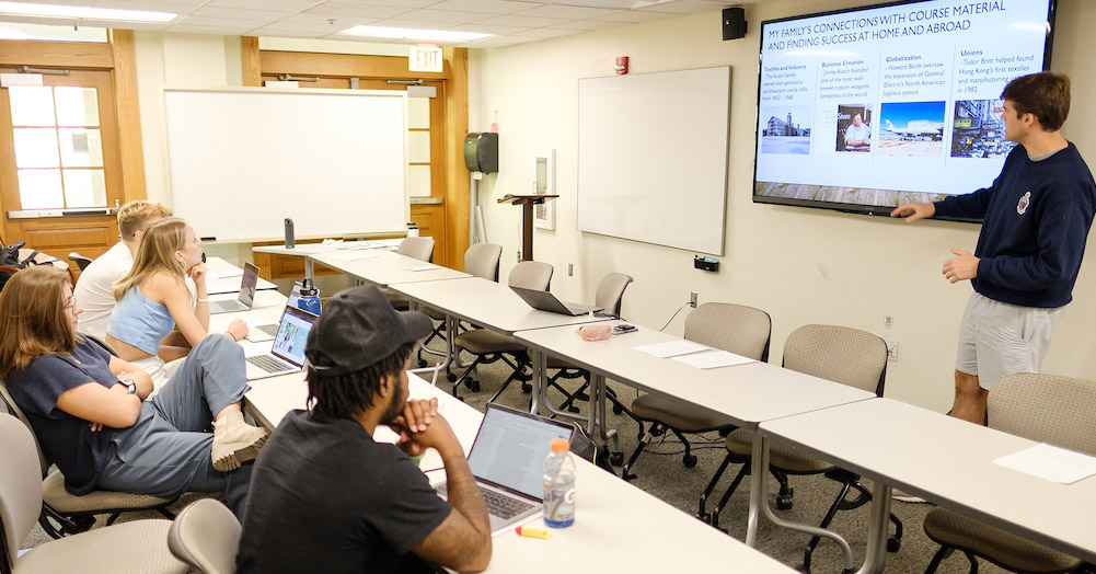 Student presents in front of screen as other students listen.