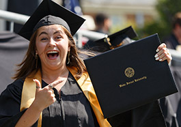 Student smiles while pointing at her diploma cover