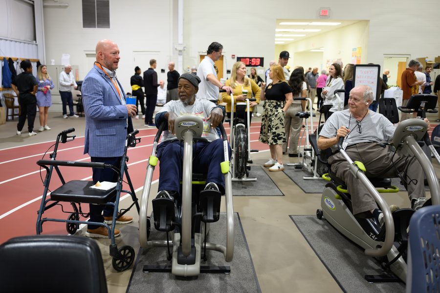 The Wake Forest University Healthy Exercise & Lifestyle Programs (HELPS) celebrates their 50th anniversary by inviting former intervention staff and students to the Clinical Research Center to meet current participants and get to know the new facility on Friday, October 17, 2025.   HELPS Program Director Jeff Katula visits with HELPS Program participant Ernie Wade, as he works out on an exercise bike.