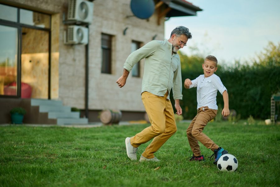 Grandfather and grandson play soccer in their backyard on a sunny day, bonding and creating lasting memories of fun and love