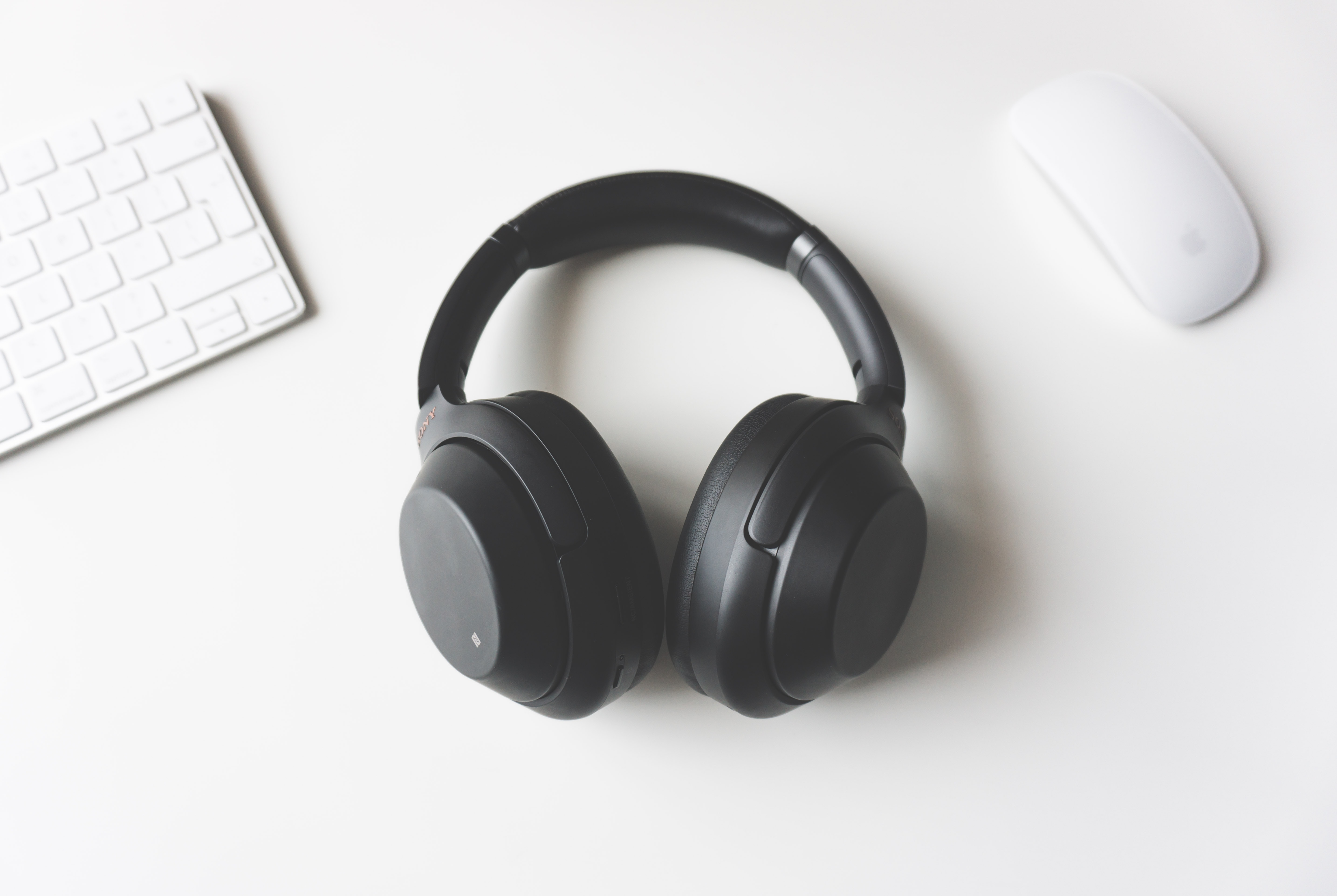 image of black headphones surrounded by a keyboard and mouse on a white background. Photo by Tomasz Gawlowski on Upsplash.