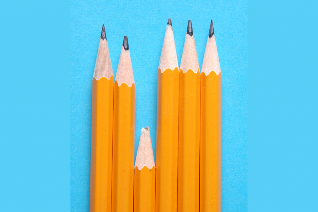 Image of 6 pencils in a row on a blue background. Five of the pencils are long and sharpened, but the third pencil in the row is short and has a broken tip.