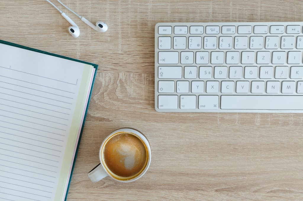Decorative image of an open notebook, cup of espresso, earbuds, and a keyboard