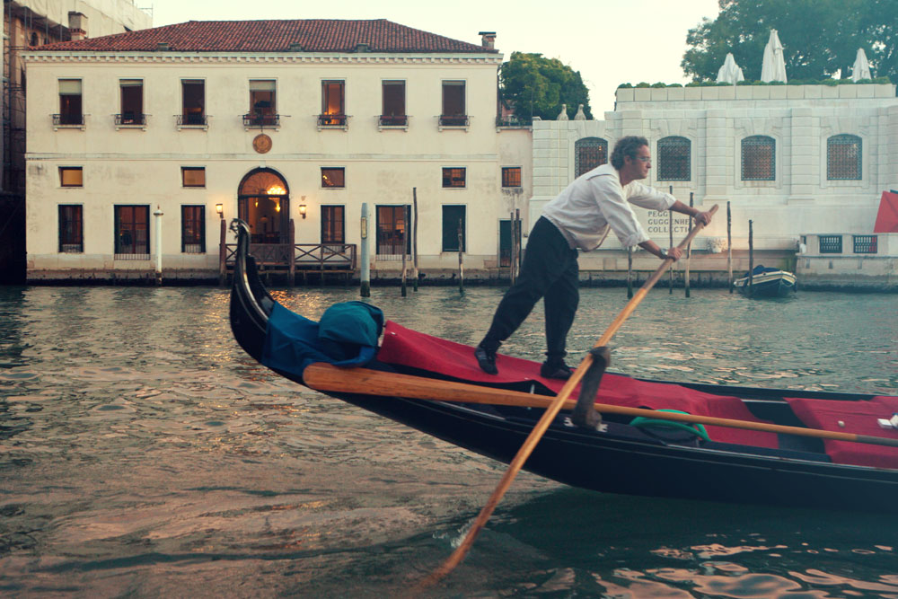 man steering a gondola in the canal in front of casa artom