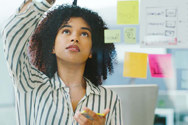 A woman looks at Post-it notes on a class wall.