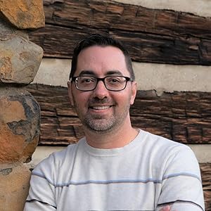 A photograph of Adam Kadlac, wearing glasses and a striped sweater.