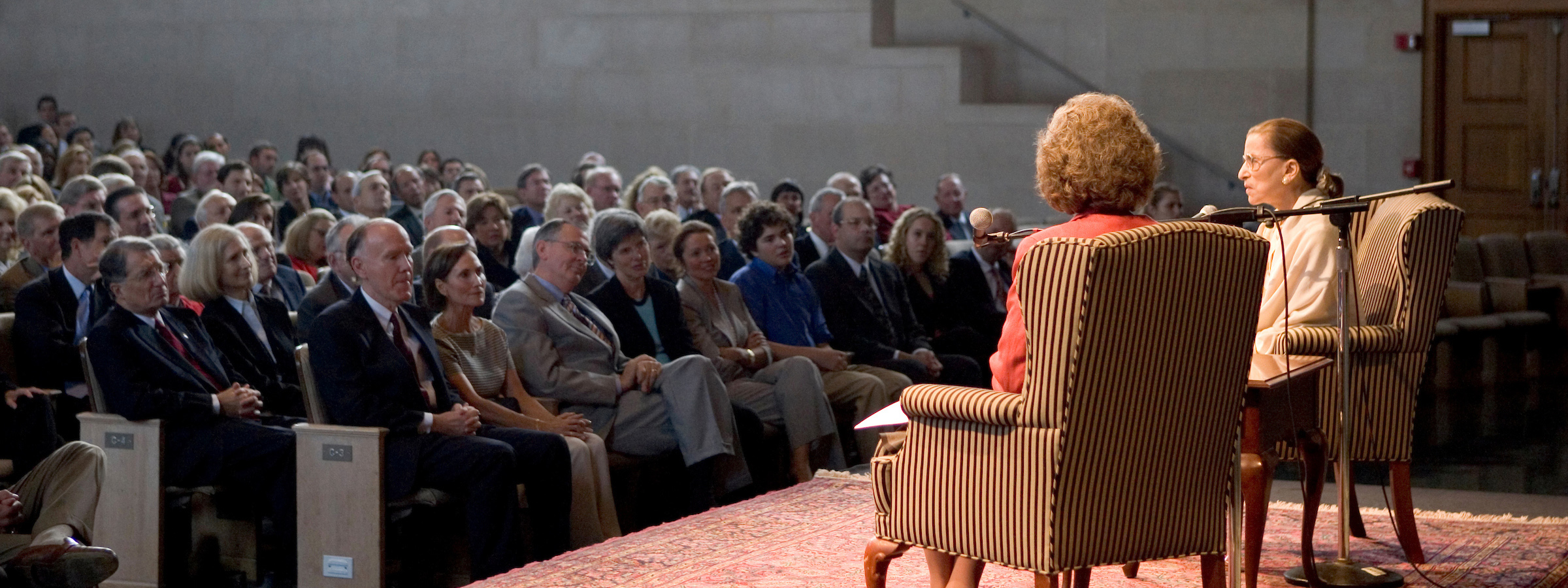 Ruth Bader Ginsburg and a host sit in wingback chairs on the stage of Wait Chapel in front of a seated crowd