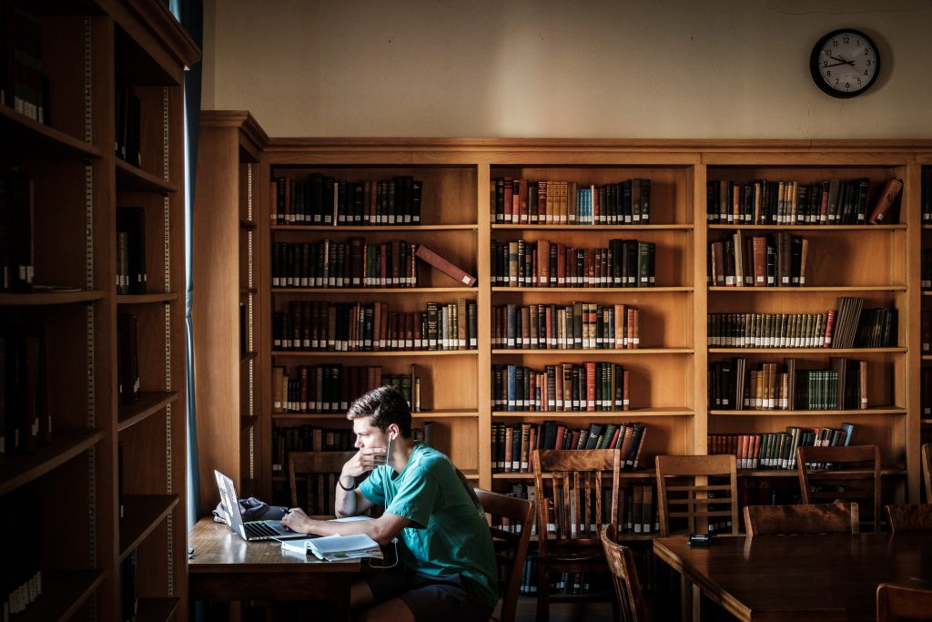 Student sits in philosophy library and works at a laptop. 