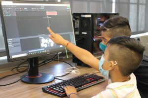 Two children pointing at a music production software on a computer.