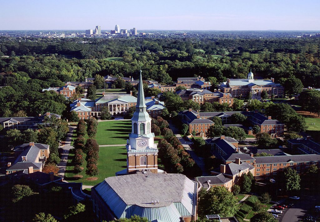 Aerial photo of Wake Forest University with the Winston Salem skyline in the background rising above the trees.