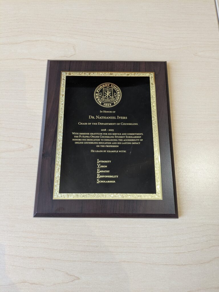 Plaque for Dr. Nate Ivers reads: In Honor of Dr. Nathaniel Ivers Chair of the Department of Counseling 2018-2025. With immense gratitude for his service and commitment, the Pi Alpha Online Counseling Student Scholarship honors his dedication to enhancing the accessibility of online counseling education and his lasting impact on the profession. He leads by example with: Integrity, Vision, Empathy, Responsibility, and Scholarship.