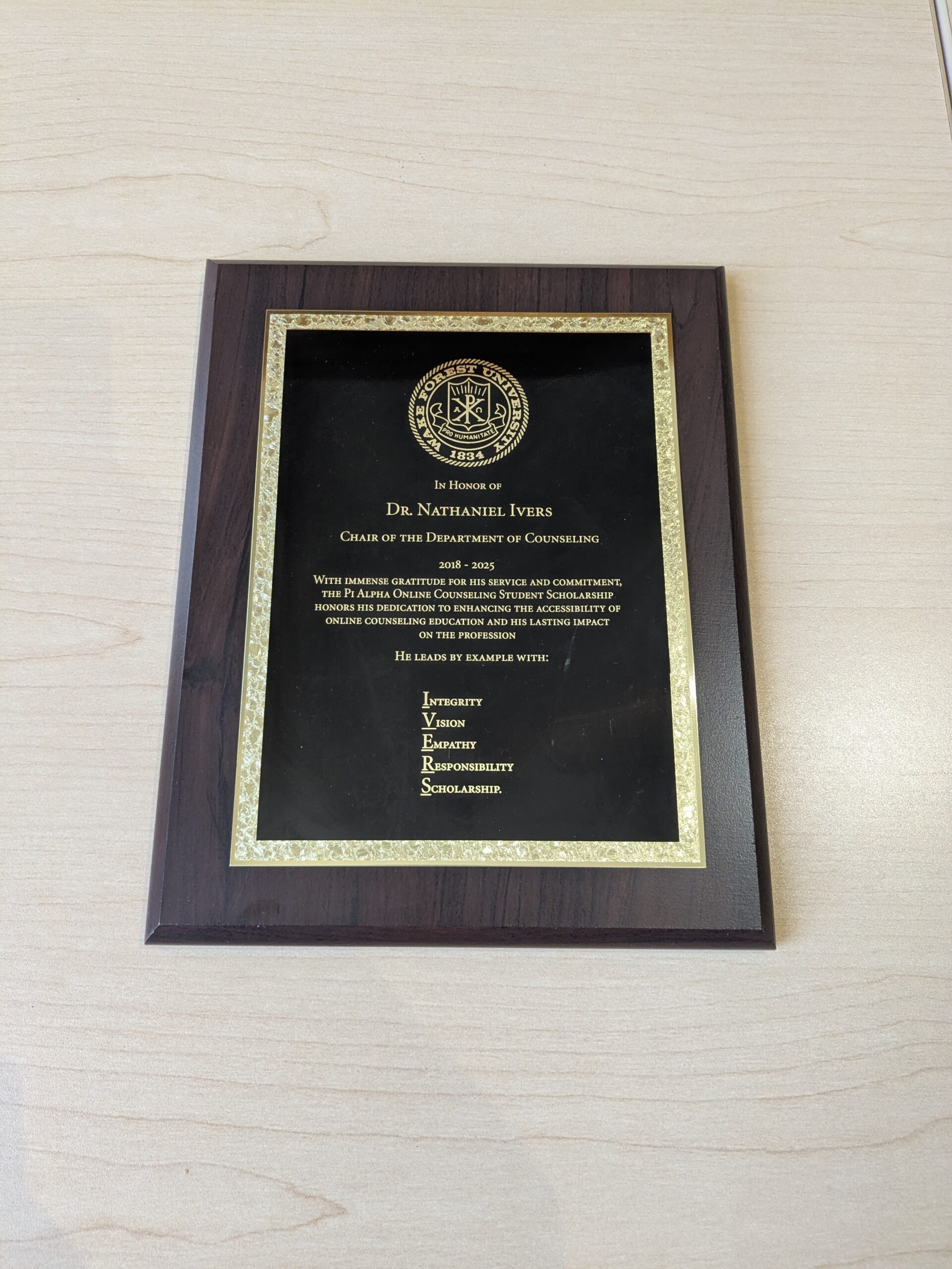 Plaque for Dr. Nate Ivers reads: In Honor of Dr. Nathaniel Ivers Chair of the Department of Counseling 2018-2025. With immense gratitude for his service and commitment, the Pi Alpha Online Counseling Student Scholarship honors his dedication to enhancing the accessibility of online counseling education and his lasting impact on the profession. He leads by example with: Integrity, Vision, Empathy, Responsibility, and Scholarship.