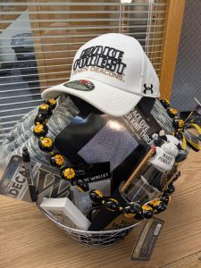 Pi Alpha Raffle Drawing. Photo of Basket #1 is 'All things Wake Forest' and includes a WFU throw, Black and gold seed pod necklace, baseball hat, pencil, pen, 2 koozies, silver and gold keychain, phone wallet, mini stuffed cow with WFU t shirt keychain, deck of cards, car decal, drinking glass with WFU seal on it. Valued at $100+.