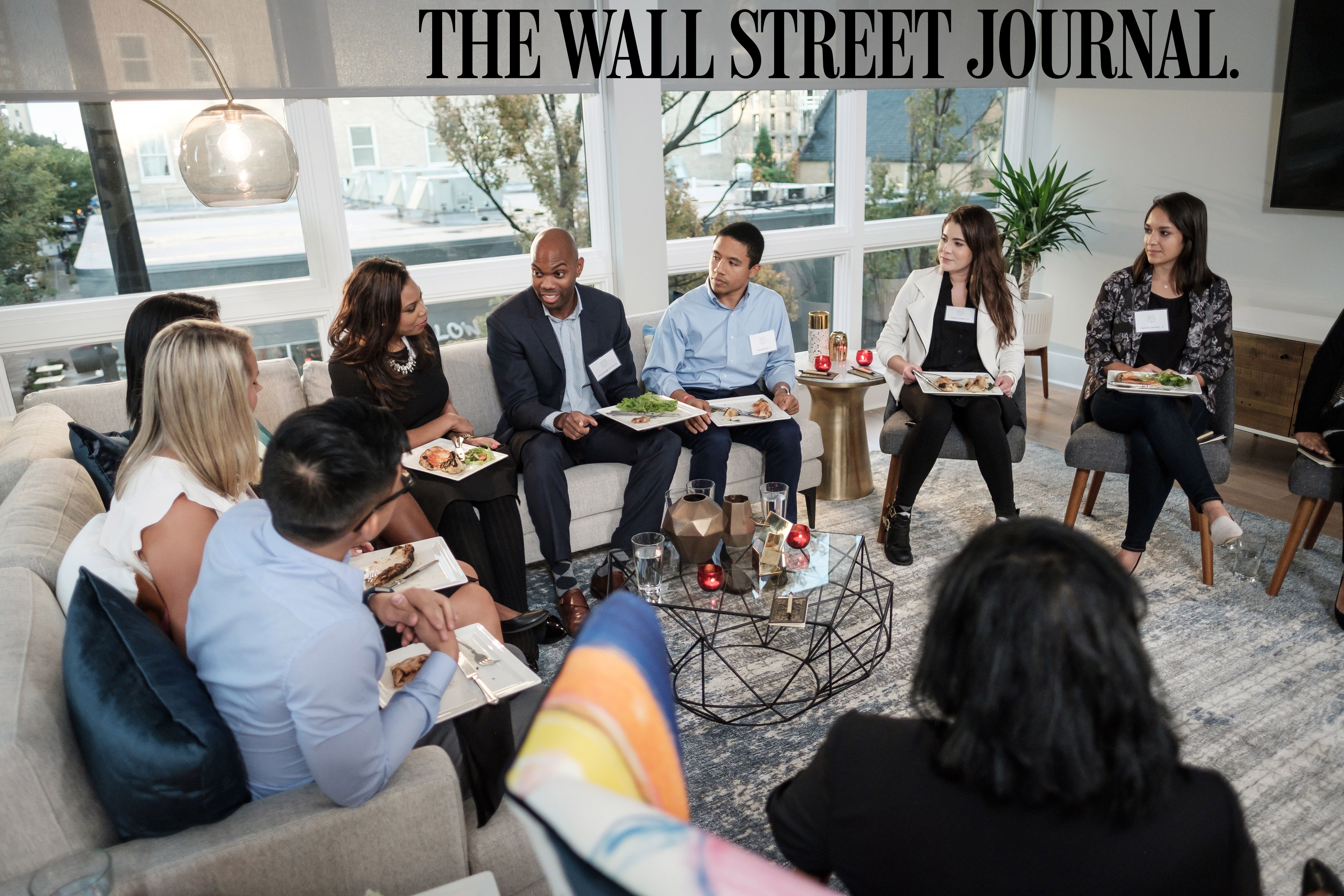 Young alumni sit and talk in a living room.