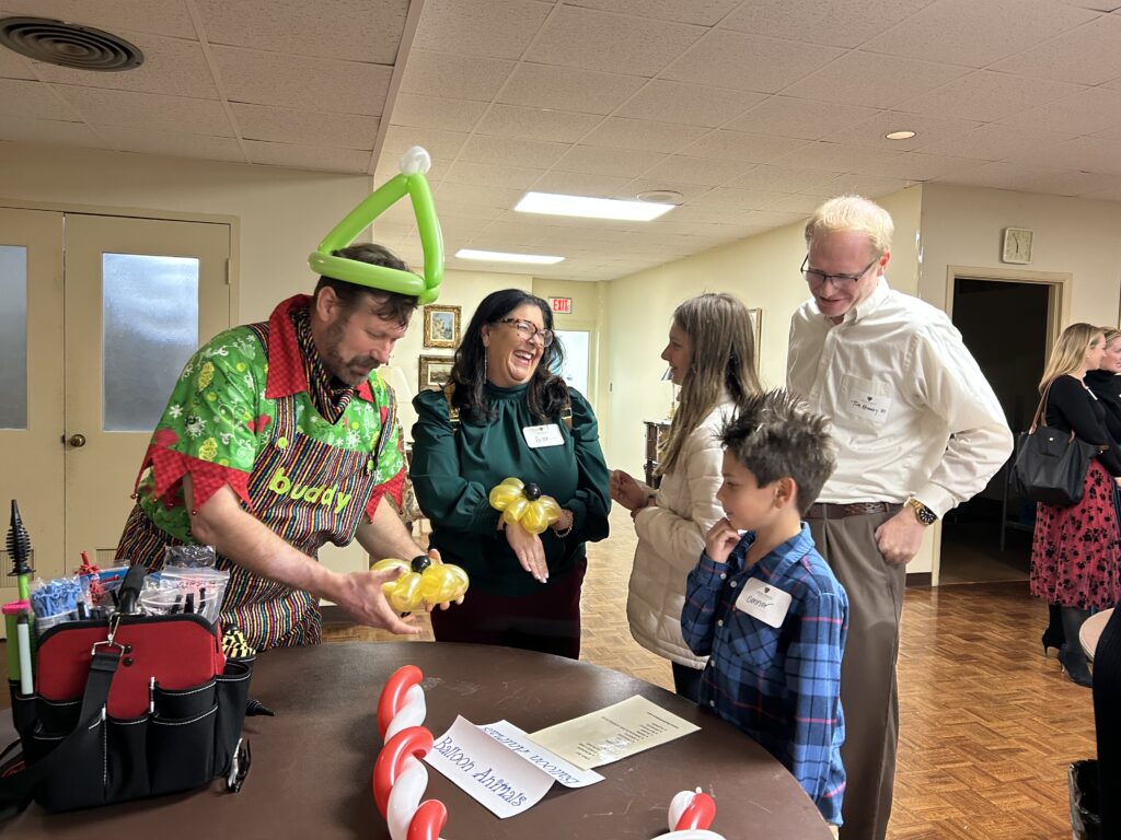 A volunteer dressed as an elf in colorful holiday attire crafts a balloon flower for guests at the WAKEAtlanta Lovefeast gathering.