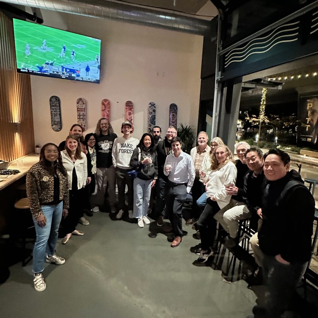 A group of Wake Forest fans stand in front of a TV showing the Wake Forest vs. Mississippi State Duke's Mayo Bowl game.